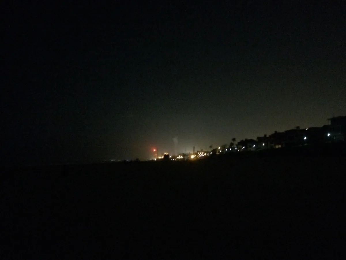 Near-total dark, with a line of streetlights along a coastal bluff and the beach in front of it unlit.