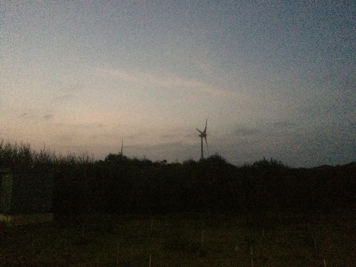 One wind turbine on a dark ridge at dusk, grain thick in the last of the light.