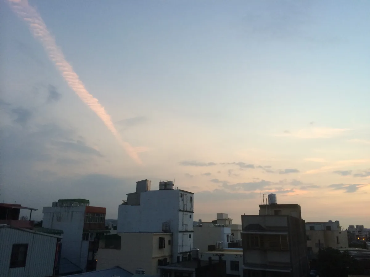 Taiwanese rooftops and water tanks at dusk, one long cloud drawn diagonally across the sky.