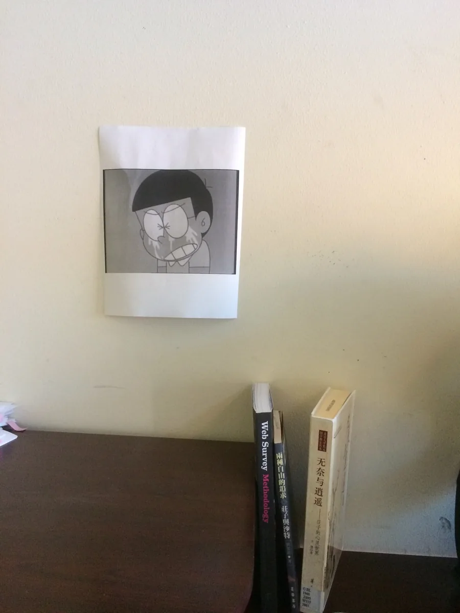 A crying cartoon panel taped above a desk, three books propped beside it, one on survey methodology.